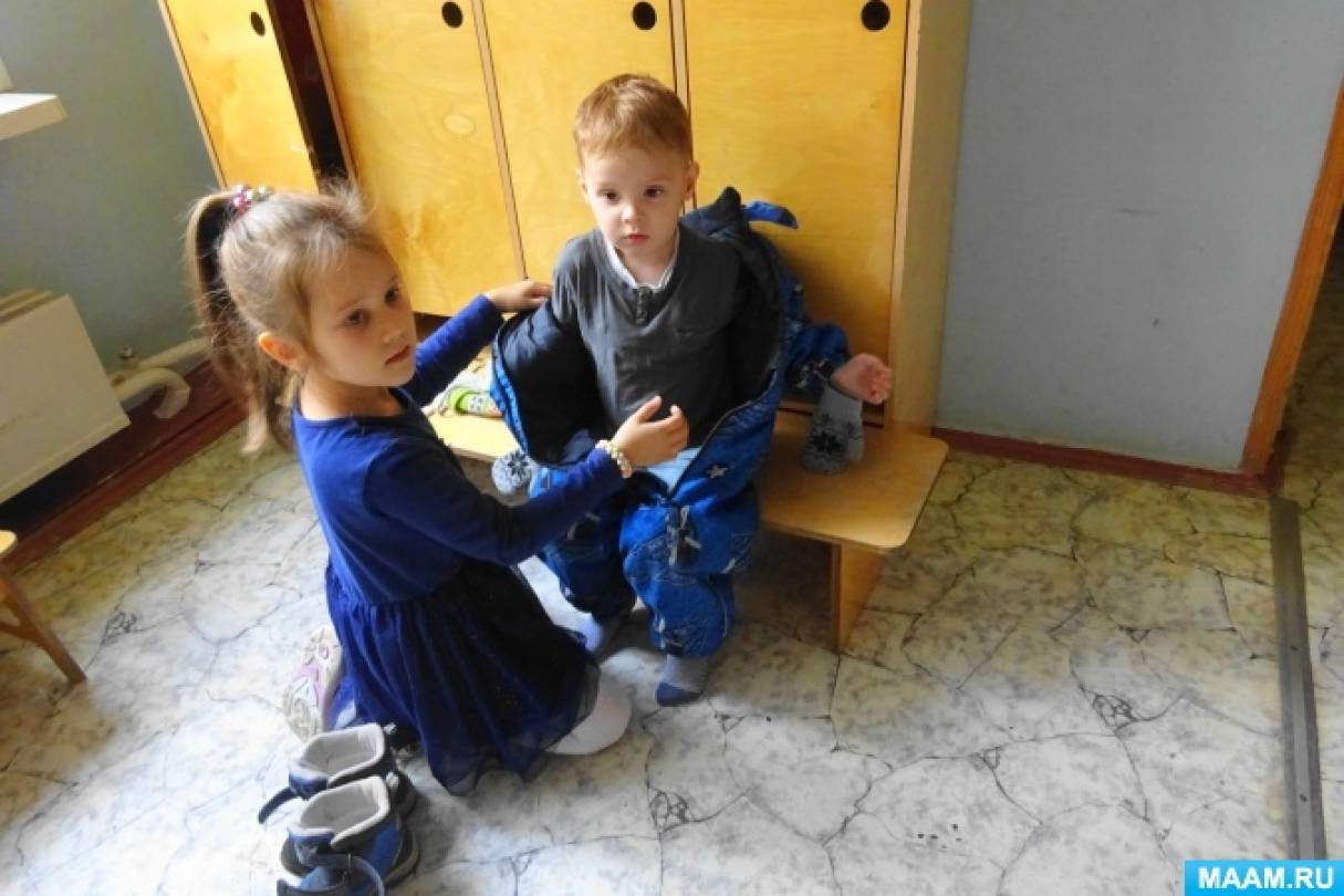 Ребенок помогает другому. Дети помогают друг другу. Дети помогают друг другу в детском саду. Старшие дети помогают младшим. Дети одеваются в детском саду.